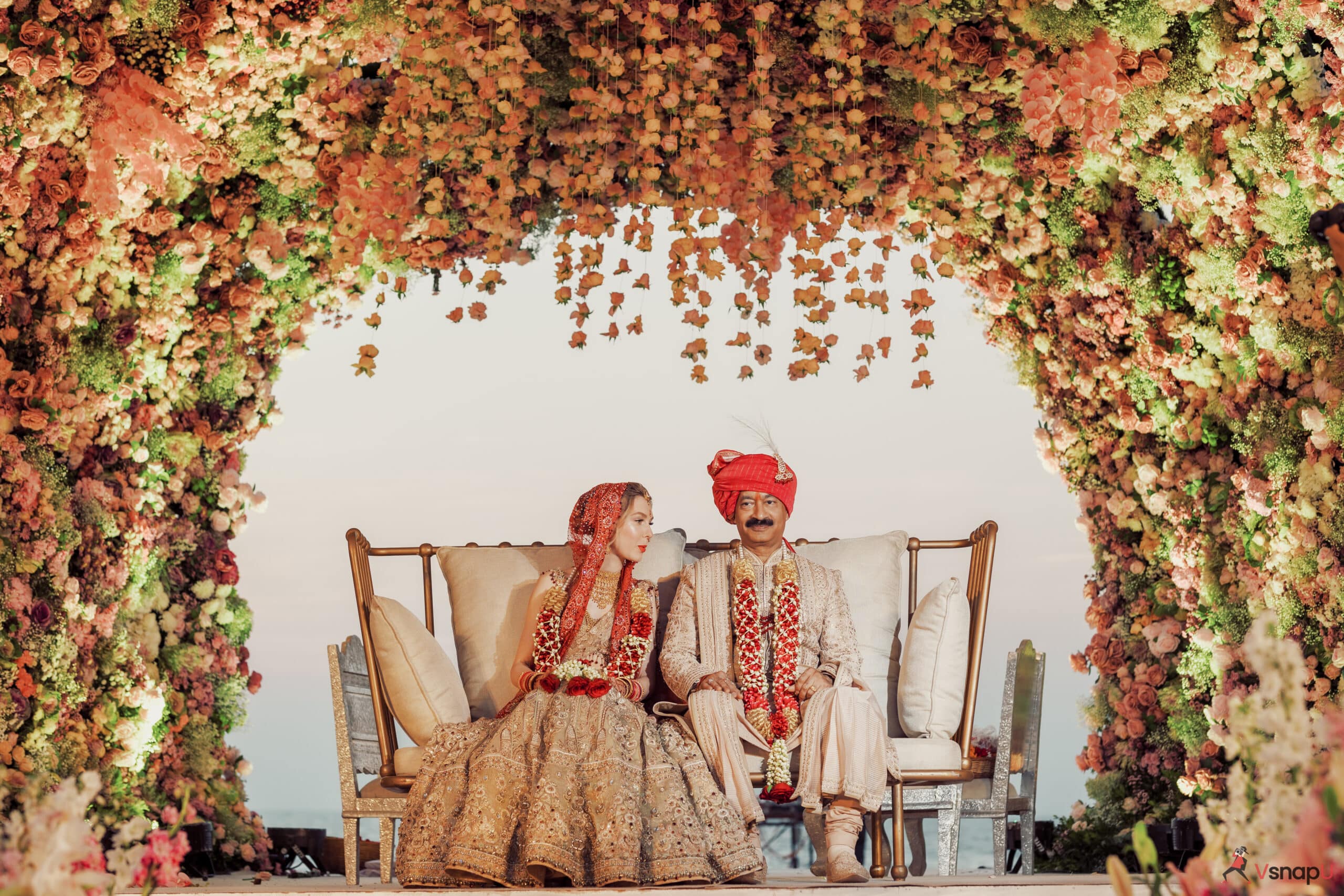 Wedding couple seated on a grand floral stage, radiating love.